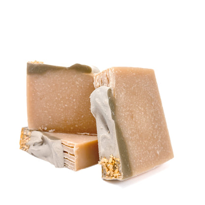 Three bars of natural-colored handmade soap, topped with a bit of green soap, and gold epsom salt dusted with gold mica.