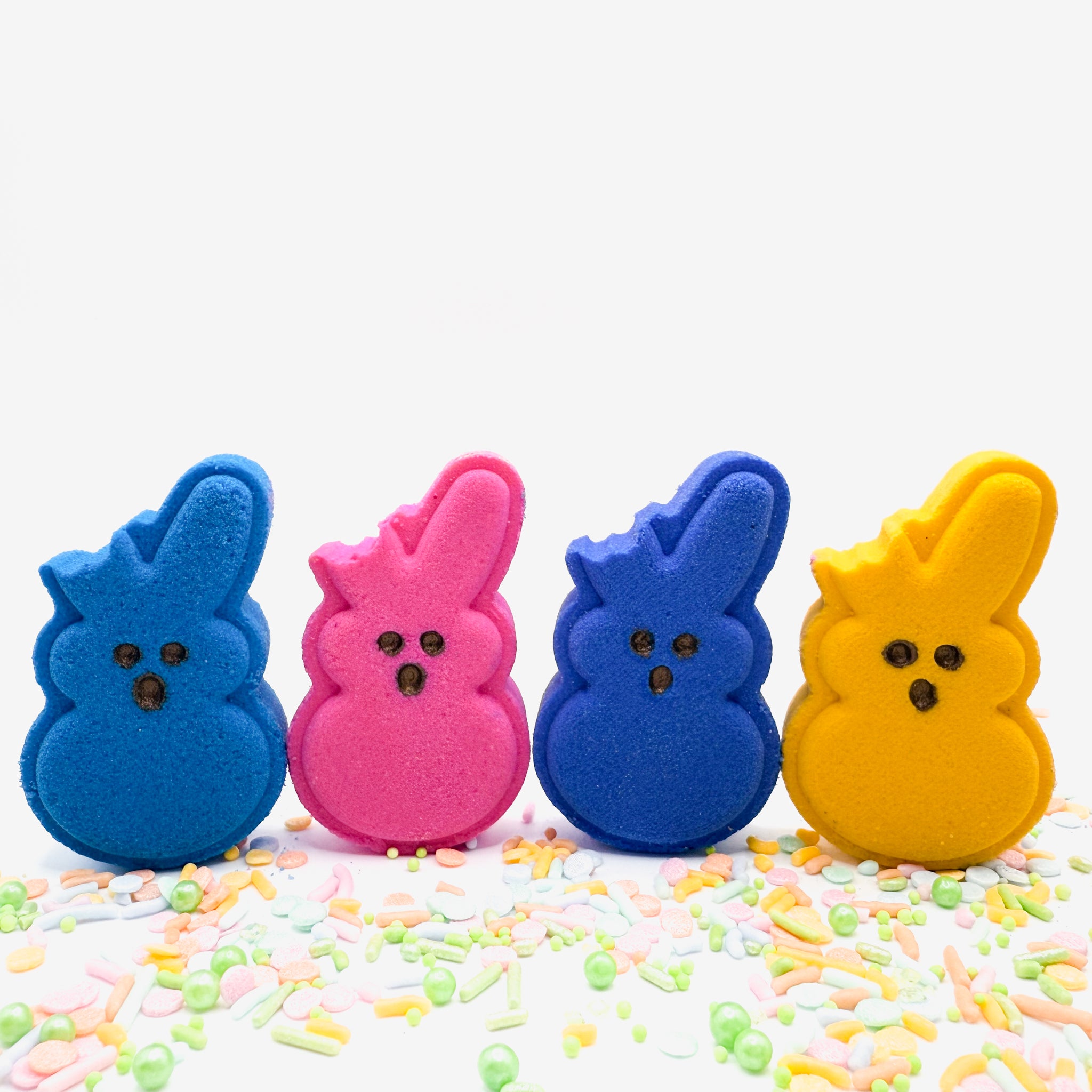 Four handmade bitten bunny bath bombs in a set by Rusted Acre Soap Co. the colors are yellow, pink, blue, and purple. The left ear is missing for a bitten look.