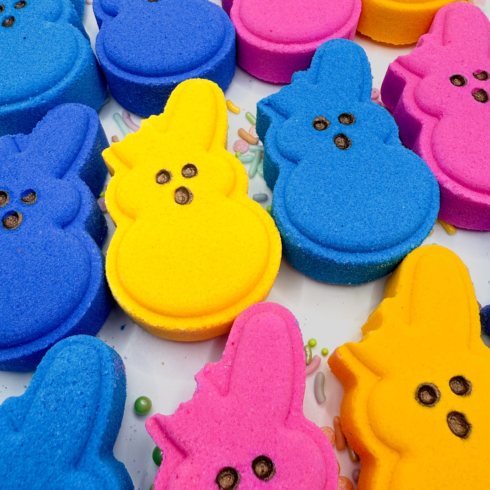 Multiple set of handmade bitten bunny bath bombs by Rusted Acre Soap Co. Colors are yellow, pink, blue, purple.