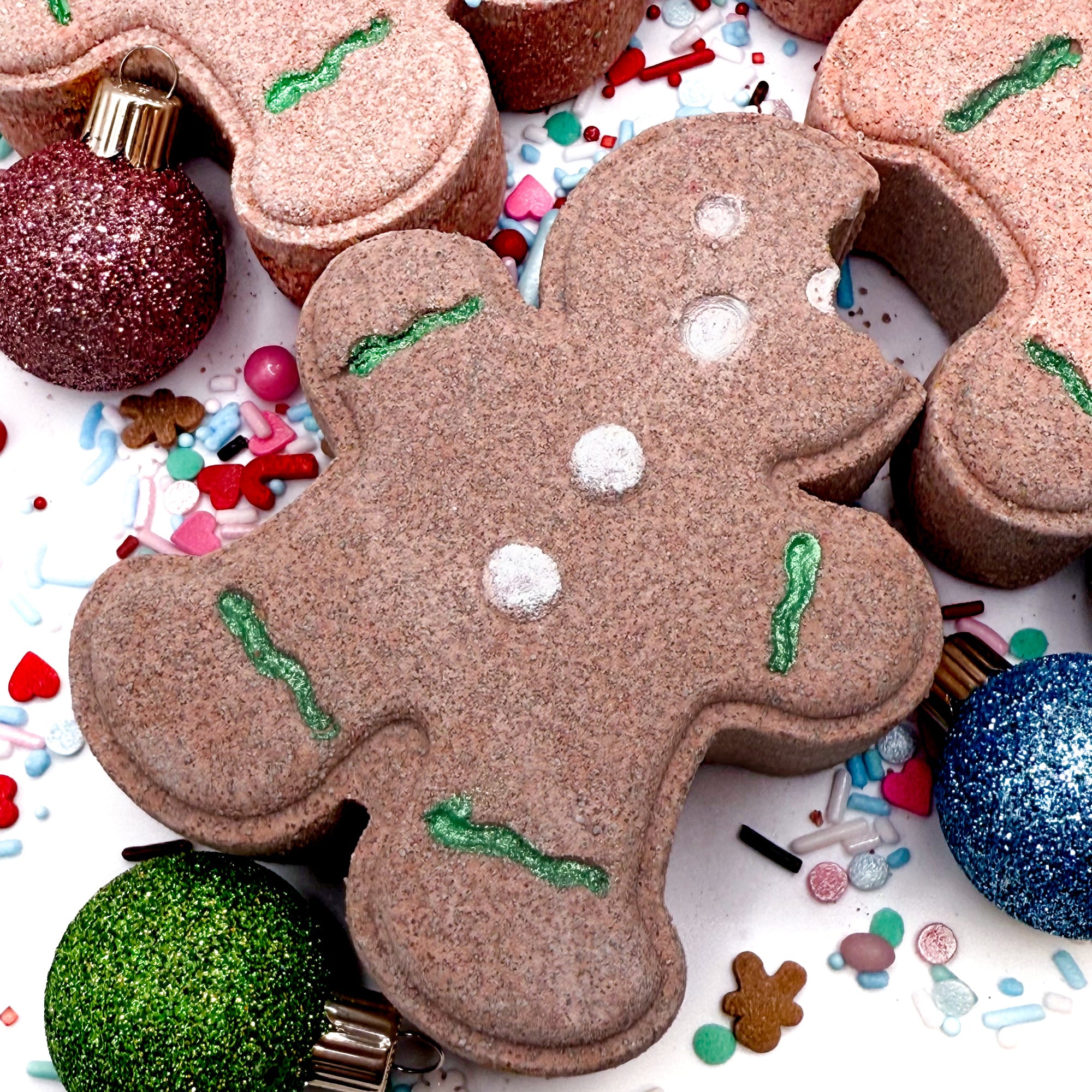 Gingerbread man-shaped cookie bath bomb with decorative elements on a festive background with ornaments and sprinkles.