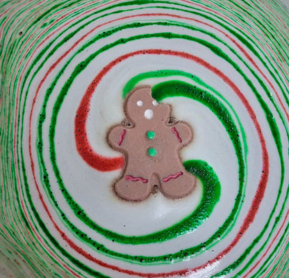 Gingerbread man bath bomb with a swirl of red, green, in the water. Handmade by Rusted Acre Soap Co.