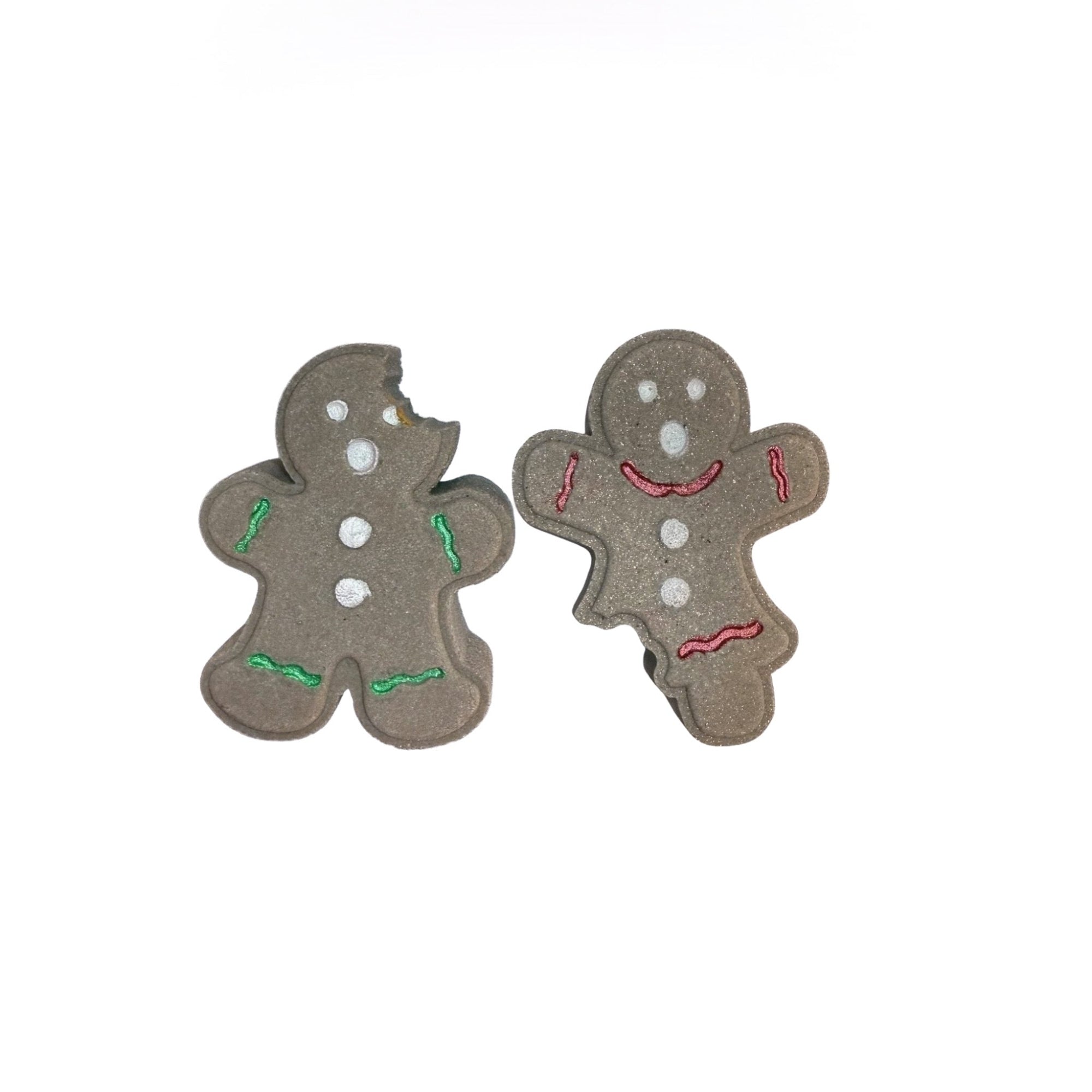 Two bitten gingerbread cookie bath bombs from Rusted Acre Soap Co. Brown in color, hand-painted white eyes, mouth, buttons. One bite out of head one out of leg.