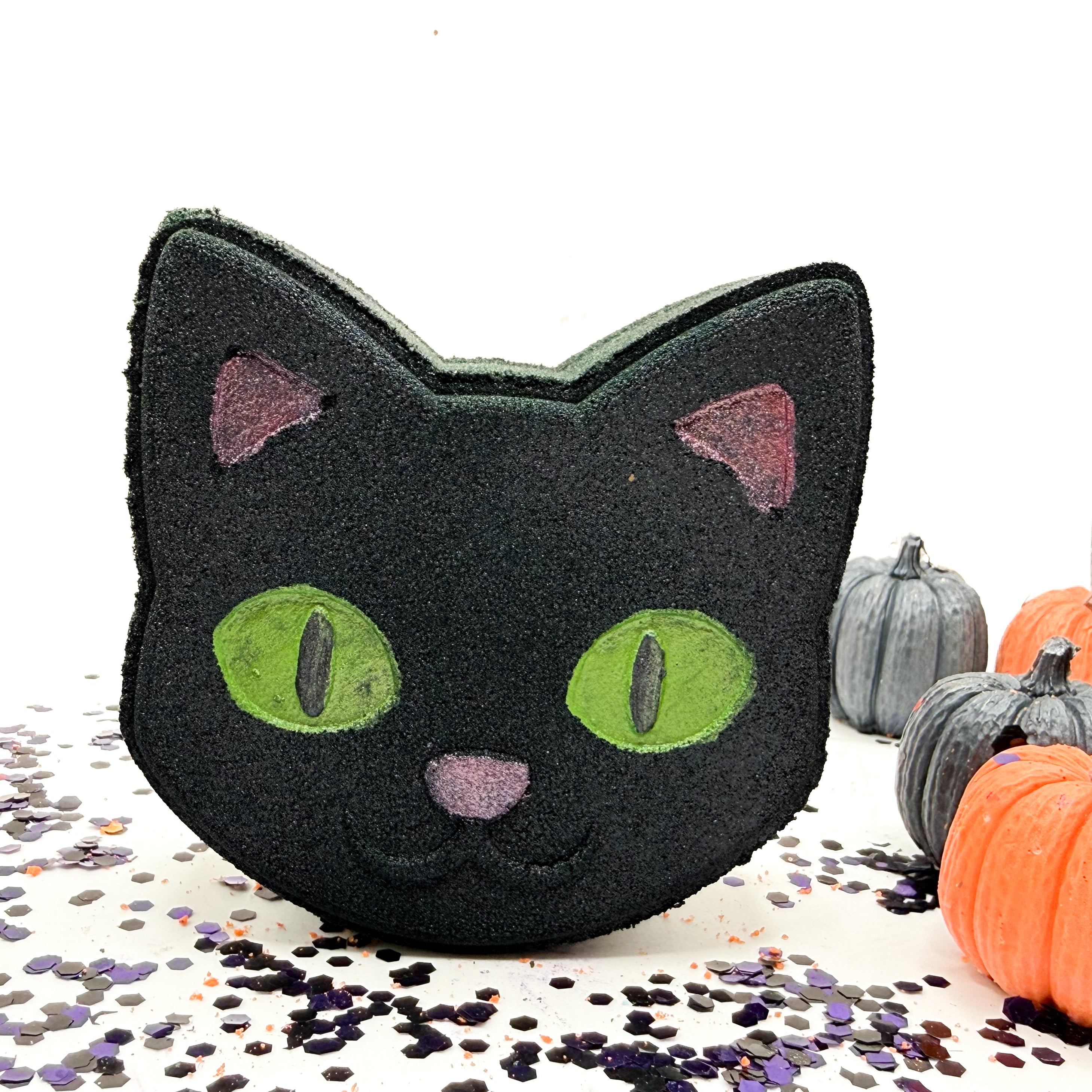 Rusted Acre Soap Co.’s handcrafted Black Cat Bath Bomb standing upright, shaped like a cat’s face with bright green eyes, pink ears, and a red nose, shown against a white background with scattered blue and purple confetti.