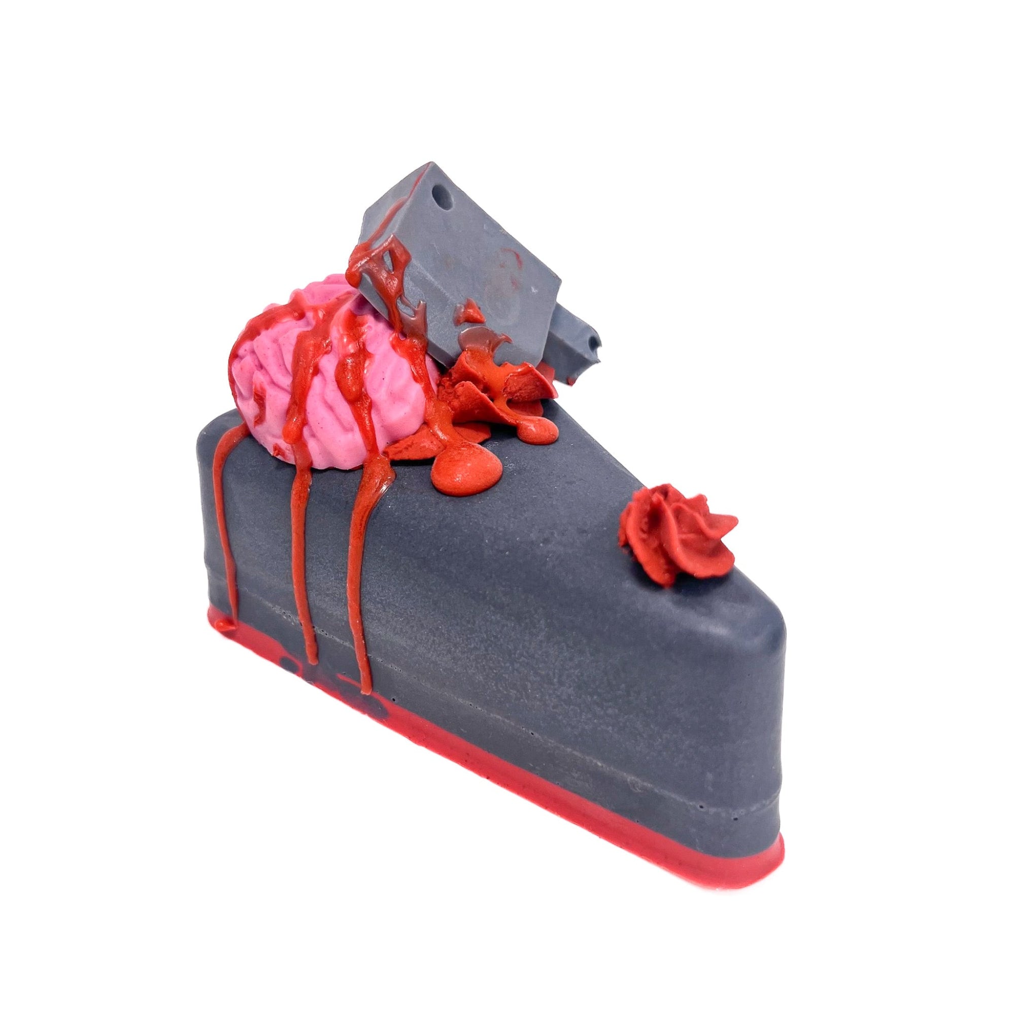 A slice of handmade black pie slice soap with red crust. Topped with a brain soap embed, a cleaver, a puff of guts, drizzled with blood soap.