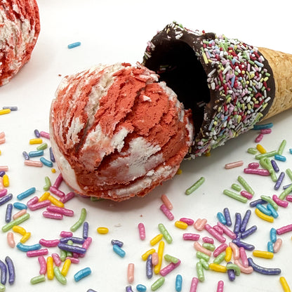 One red and white cherry almond scented bubble bath scoop handmade by Rusted Acre Soap Co. Scoop looks like an ice cream scoop. White background with sprinkles and ice cream cone prop on a white background. 
