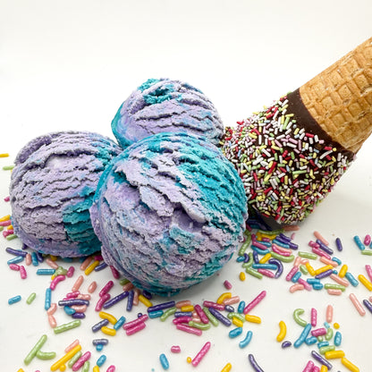 Three purple and blue mermaid kiss scented bubble bath scoops handmade by Rusted Acre Soap Co. Scoop looks like an ice cream scoop. White background with sprinkles and ice cream cone prop on a white background. 