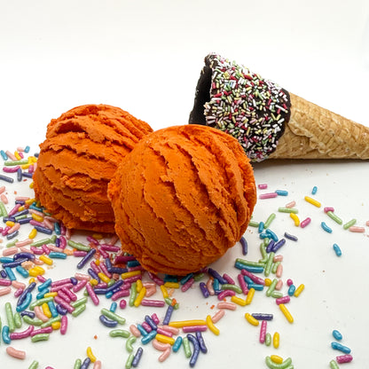 Two orange pumpkin spice scented bubble bath scoop handmade by Rusted Acre Soap Co. Scoop looks like an ice cream scoop. White background with sprinkles and ice cream cone prop on a white background. 