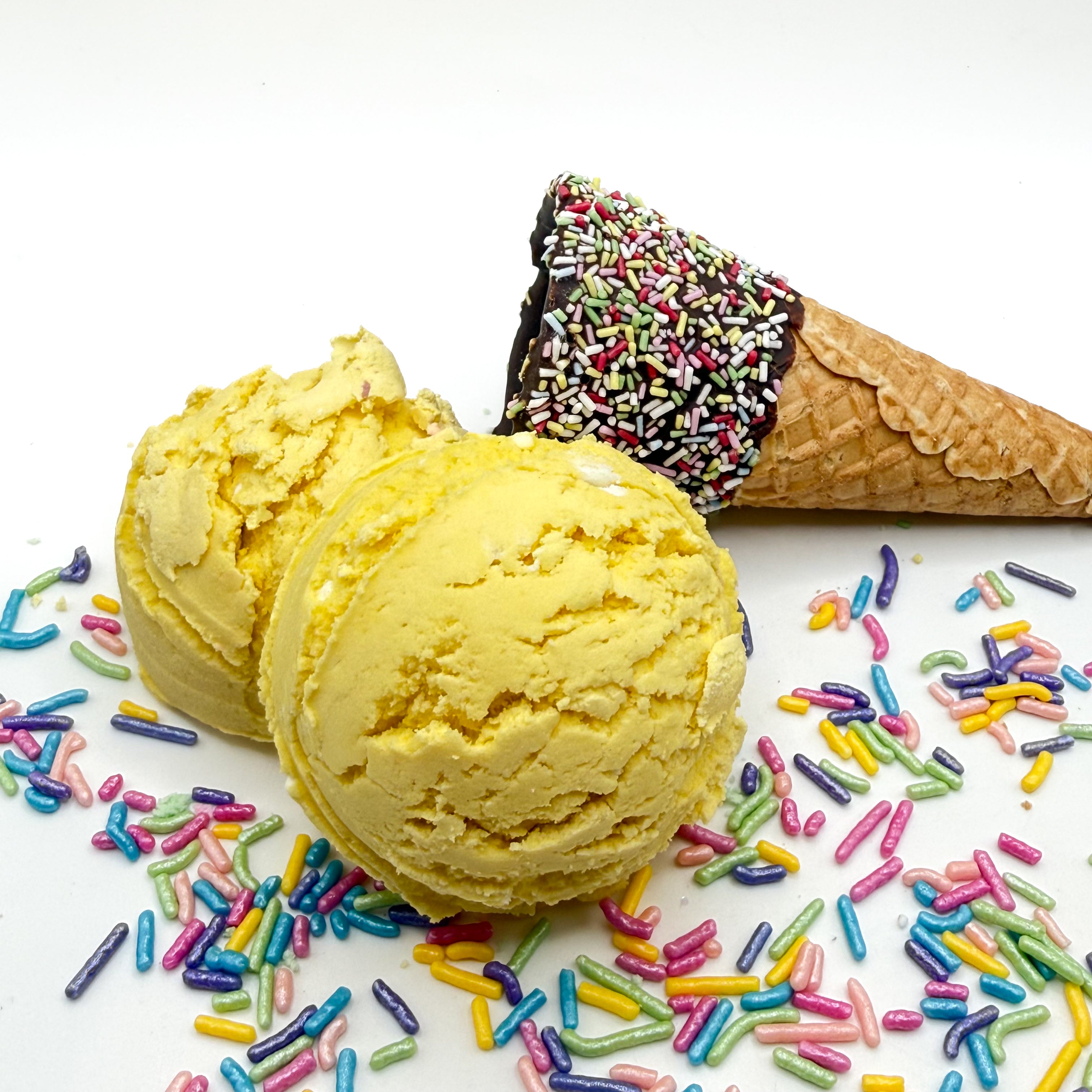 Two lemon cupcake bubble bath scoops handmade by Rusted Acre Soap Co. Scoops look like yellow ice cream scoops with sprinkles and ice cream cone prop on a white background. 