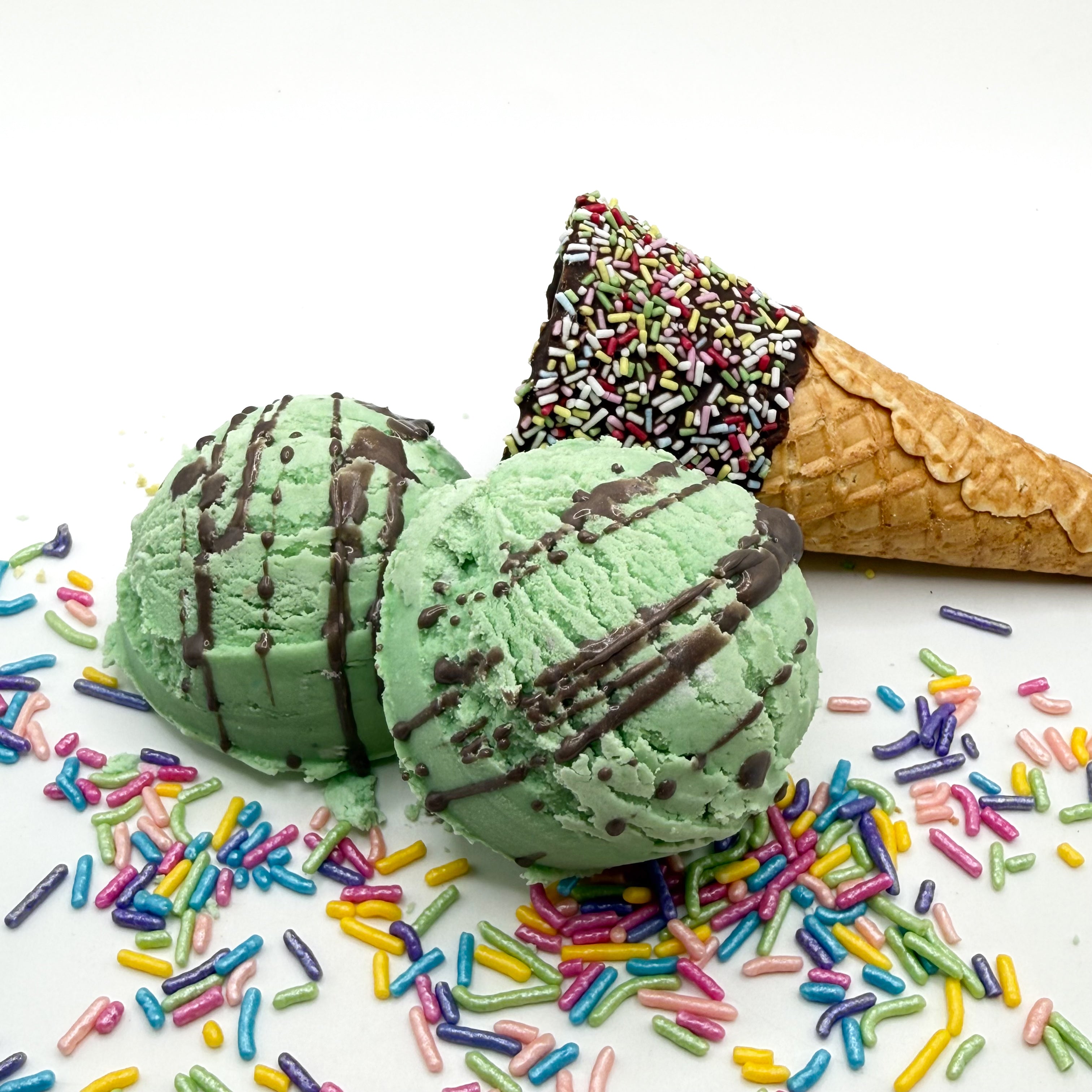 Two mint chocolate chip bubble bath scoops handmade by Rusted Acre Soap Co. Scoops look like mint green and chocolate chip ice cream scoops with sprinkles and ice cream cone prop on a white background. 
