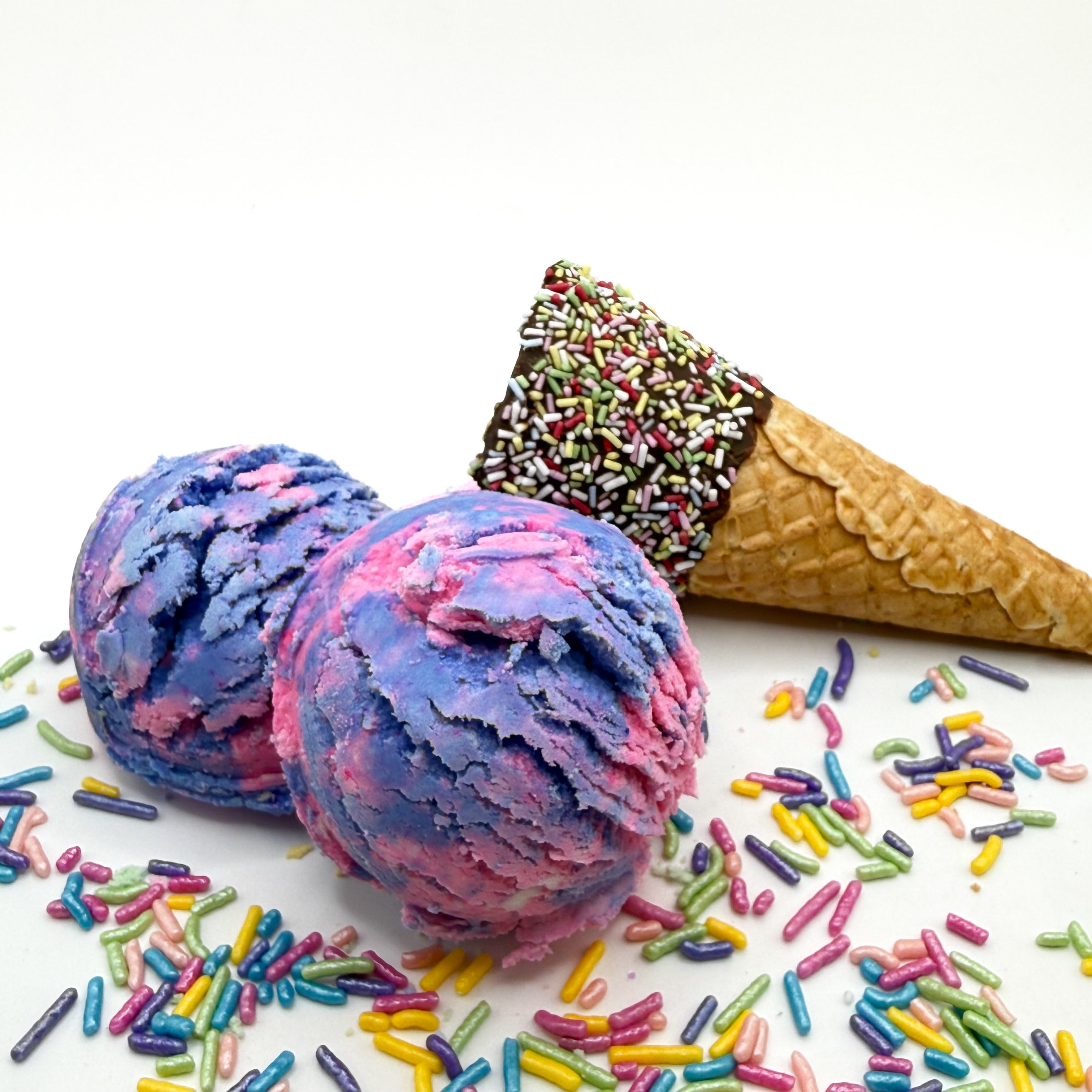 Two Raspberry Vanilla bubble bath scoops handmade by Rusted Acre Soap Co. Scoops look like pink and purple ice cream scoops with sprinkles and ice cream cone prop on a white background. 