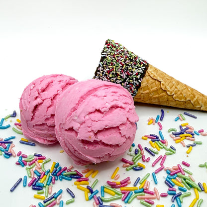 Two Strawberries and cream bubble bath scoops handmade by Rusted Acre Soap Co. Scoops look like pink ice cream scoops with sprinkles and ice cream cone prop on a white background. 