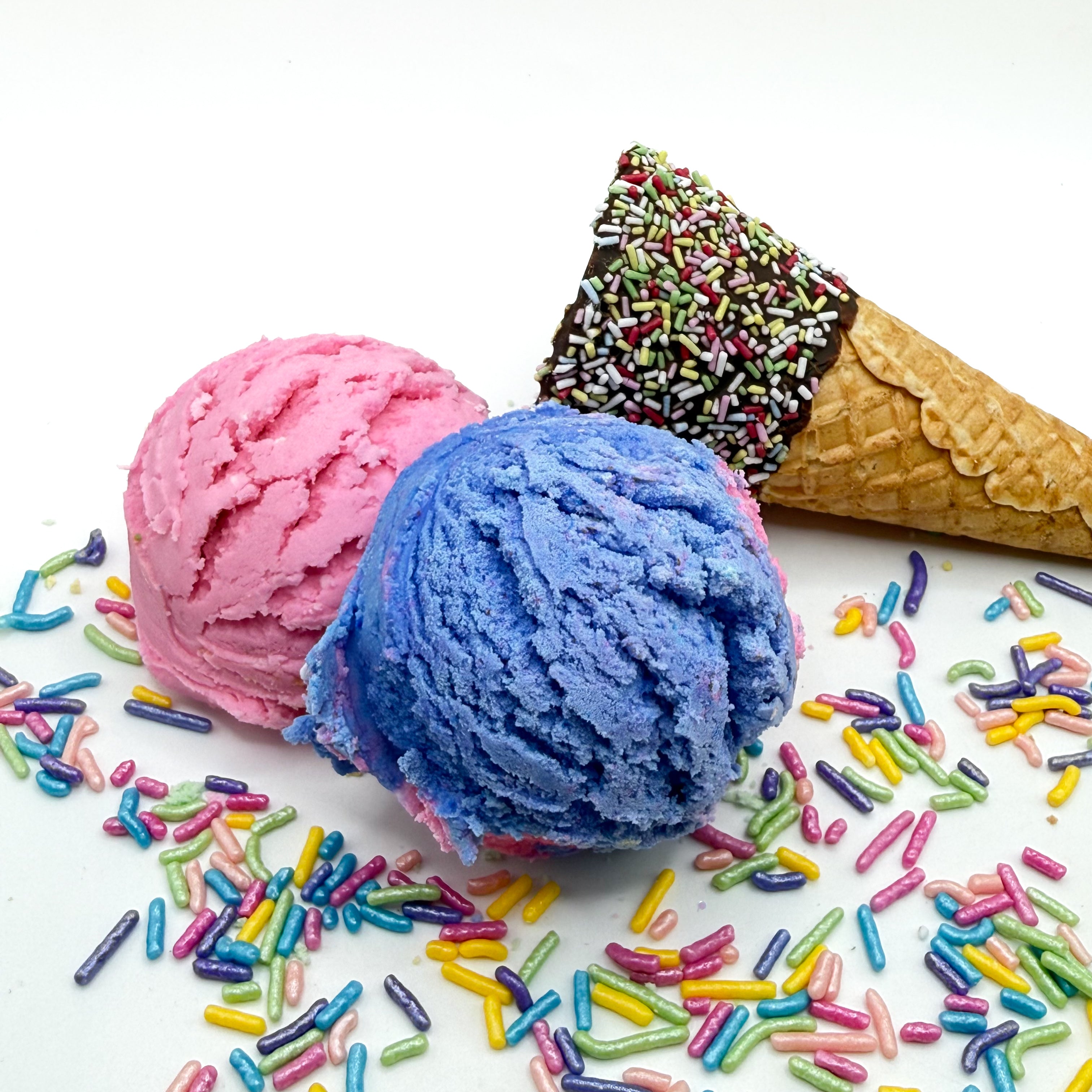 Two surprise bubble bath scoops handmade by Rusted Acre Soap Co. Scoops look like pink and purple ice cream scoops with sprinkles and ice cream cone prop on a white background. 