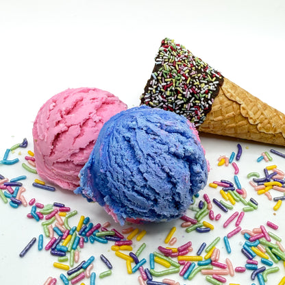 Two surprise bubble bath scoops handmade by Rusted Acre Soap Co. Scoops look like pink and purple ice cream scoops with sprinkles and ice cream cone prop on a white background. 
