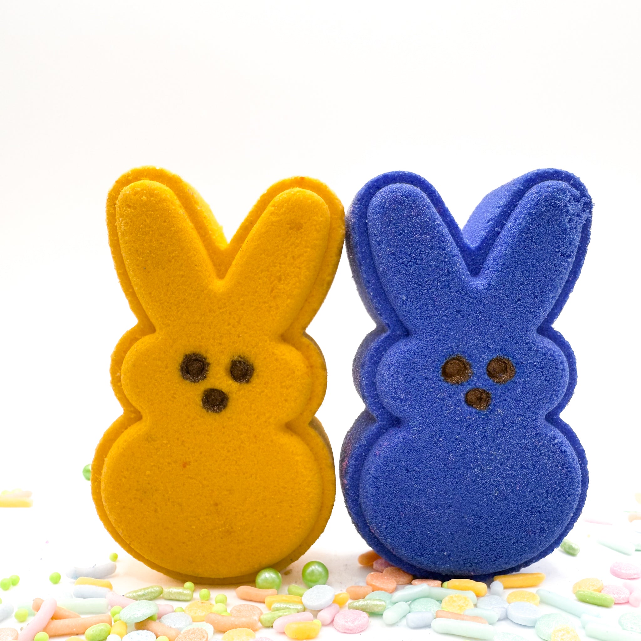 Two handmade bunny bath bombs from Rusted Acre Soap Co. One yell and one blue with hand-painted brown eyes. Displayed with pastel sprinkles.