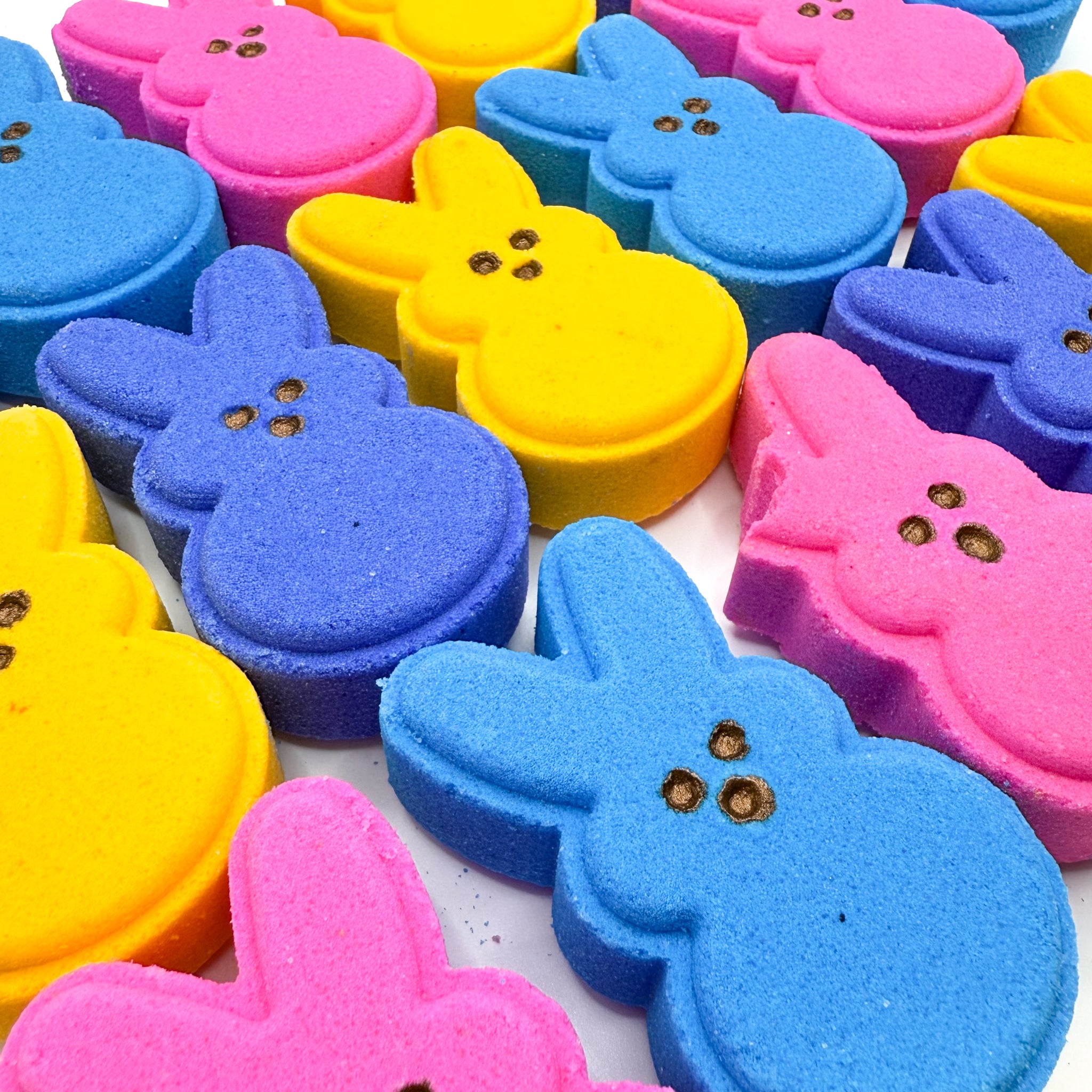 Multiple bunny bath bomb sets handmade by Rusted Acre Soap Co. Colors are pink, purple, blue, and yellow. One bitten ear.