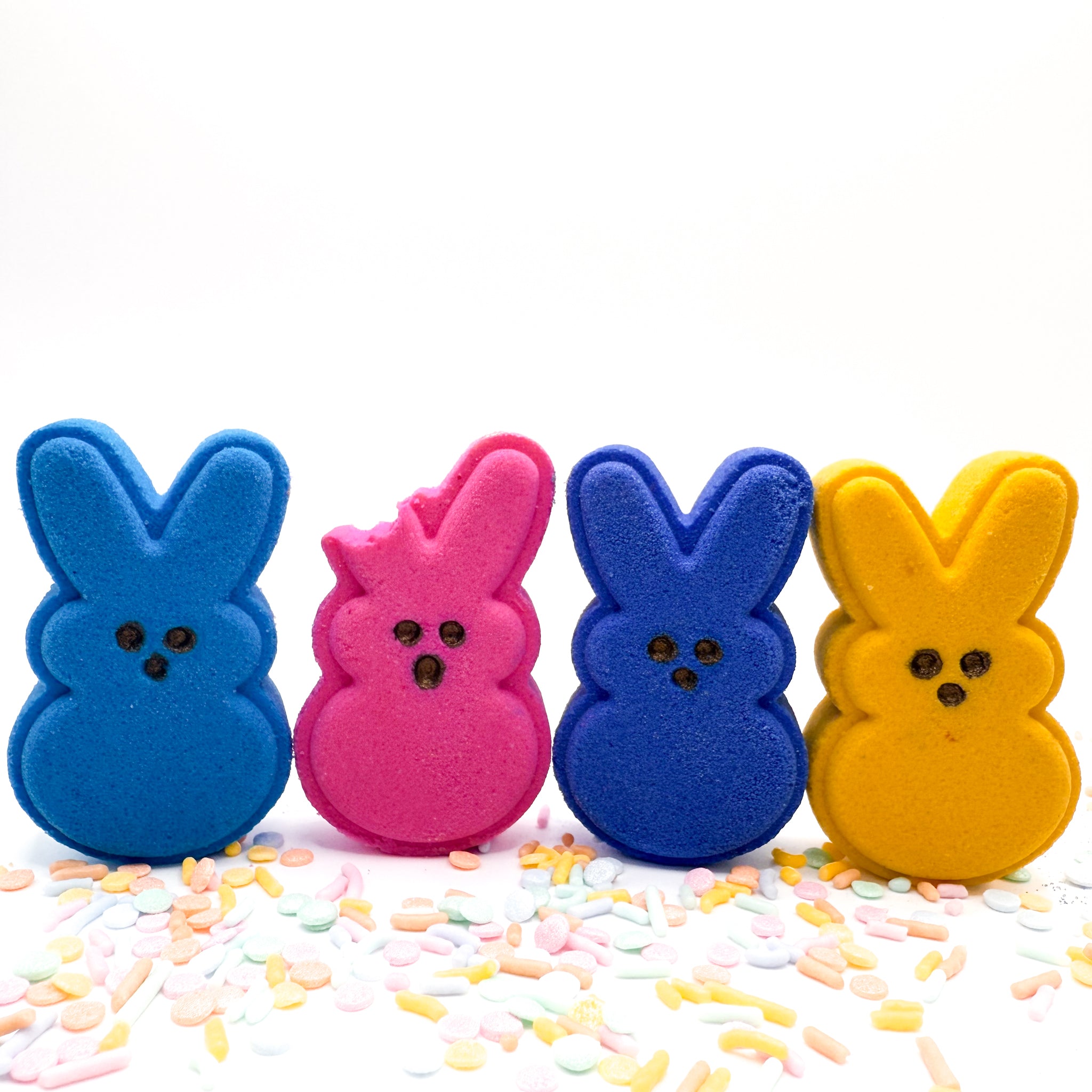 A set of four handmade bunny bath bombs from Rusted Acre Soap Co. One has a bite out of its ear. Colors are blue, pink, purple, yellow.