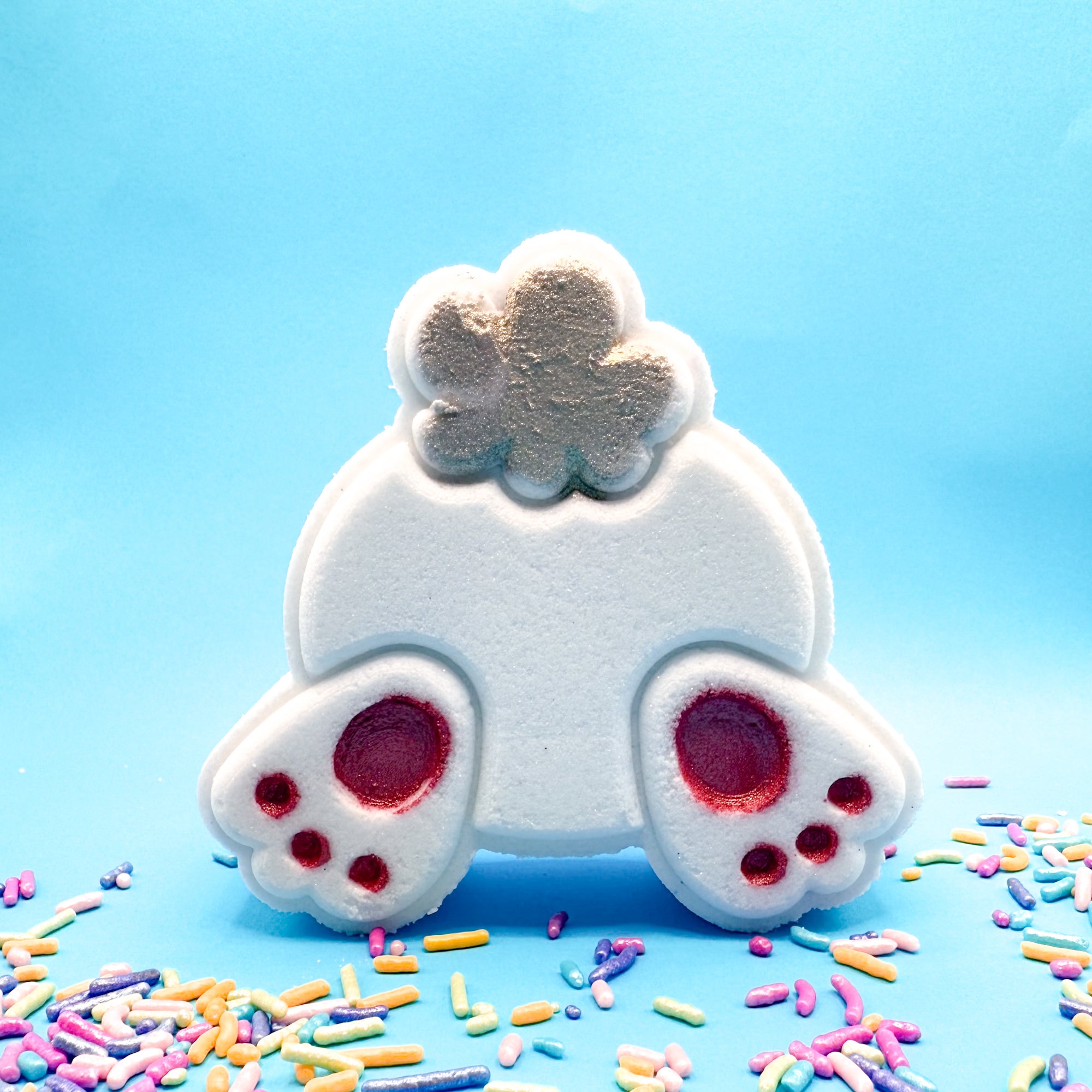 Hand painted white bunny butt bath bomb with pink feet pads, sparkly tail on a blue background with Easter sprinkles. 
