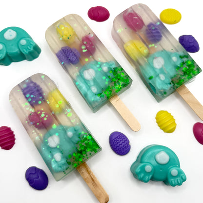 Three Easter popsicle shaped soap bars with a teal bunny butt and egg soaps embedded inside on a white background. Handmade by Rusted Acre Soap Co.