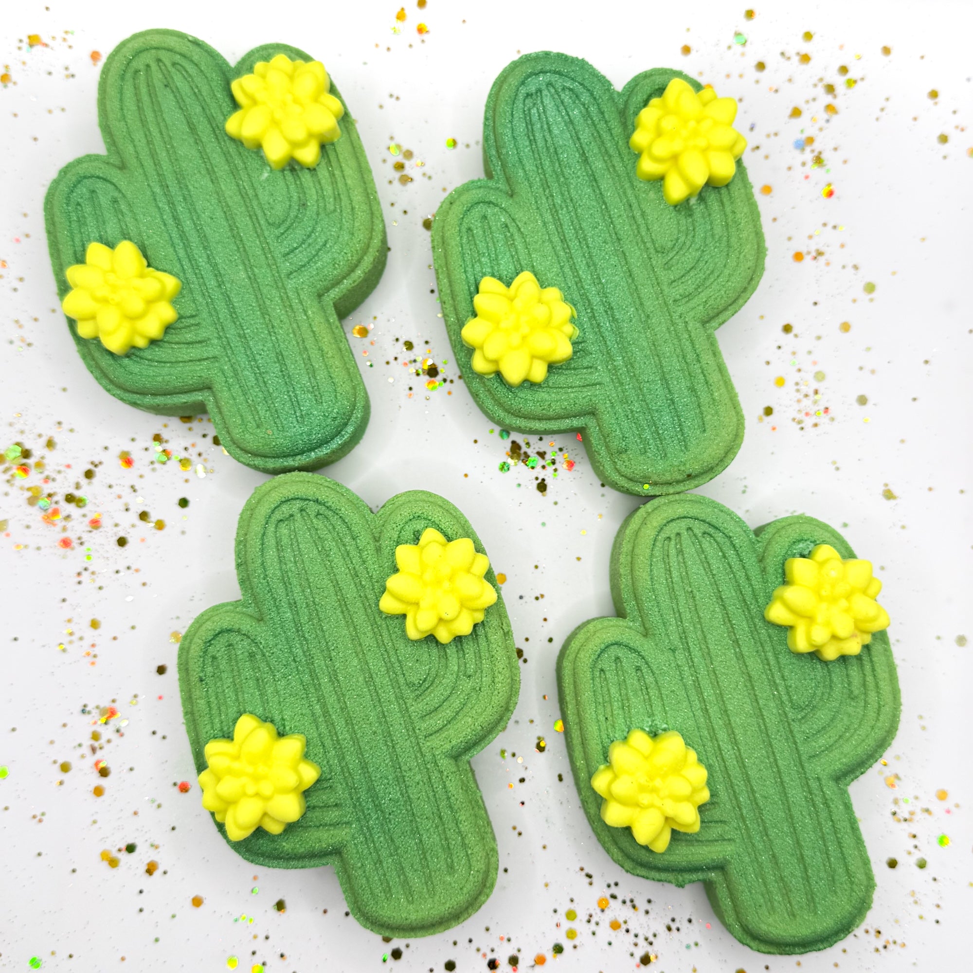 Four green cactus shaped bath bombs with yellow flowers on a white background. 
