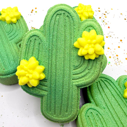 One green cactus shaped bath bomb standing up with other lying. Each adorned with two 
 light yellow cactus flower mini soap.