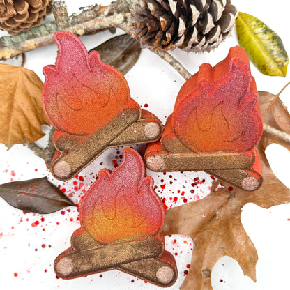 Three hand painted campfire bath bombs with leaves, sticks and pinecones on a white background.