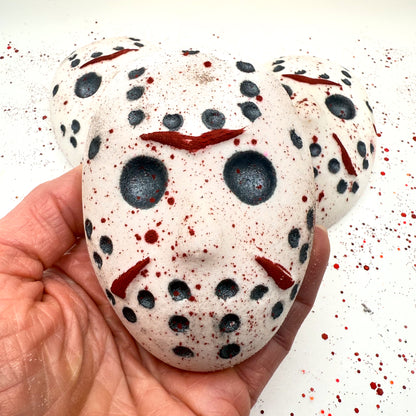 Close-up of Camp Slasher horror bath bomb being held, showing the painted red slashes and black mask holes with splatter design. Made by Rusted Acre Soap Company 
