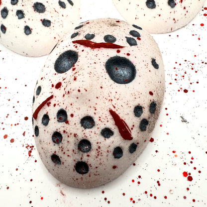 Angled view of Camp Slasher bath bomb laying flat, showcasing detailed red and black painted mask design with scattered blood splatter.