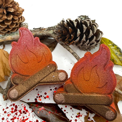 Two campfire shaped bath bombs with pine cones sticks, and leaves on a decorated white background.