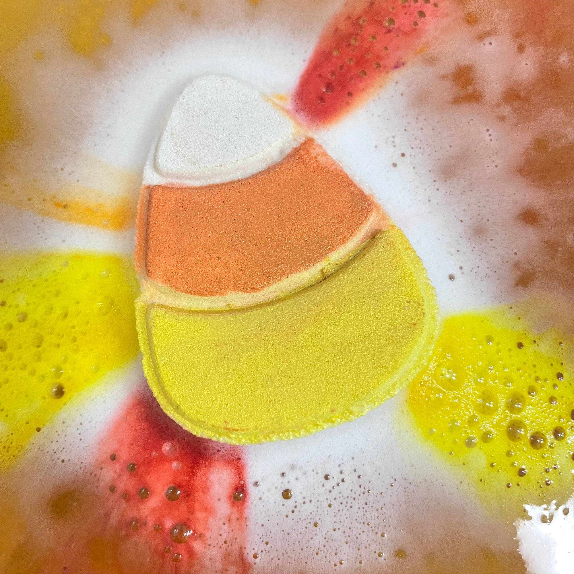 Candy corn-shaped bath bomb in a tub fizzing with colorful foam.