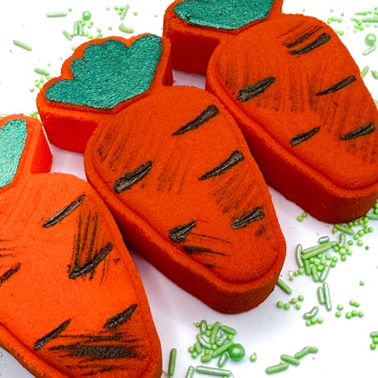 Three hand painted orange Carrot  bath bombs with green tops and “dirt” paint on a white background.