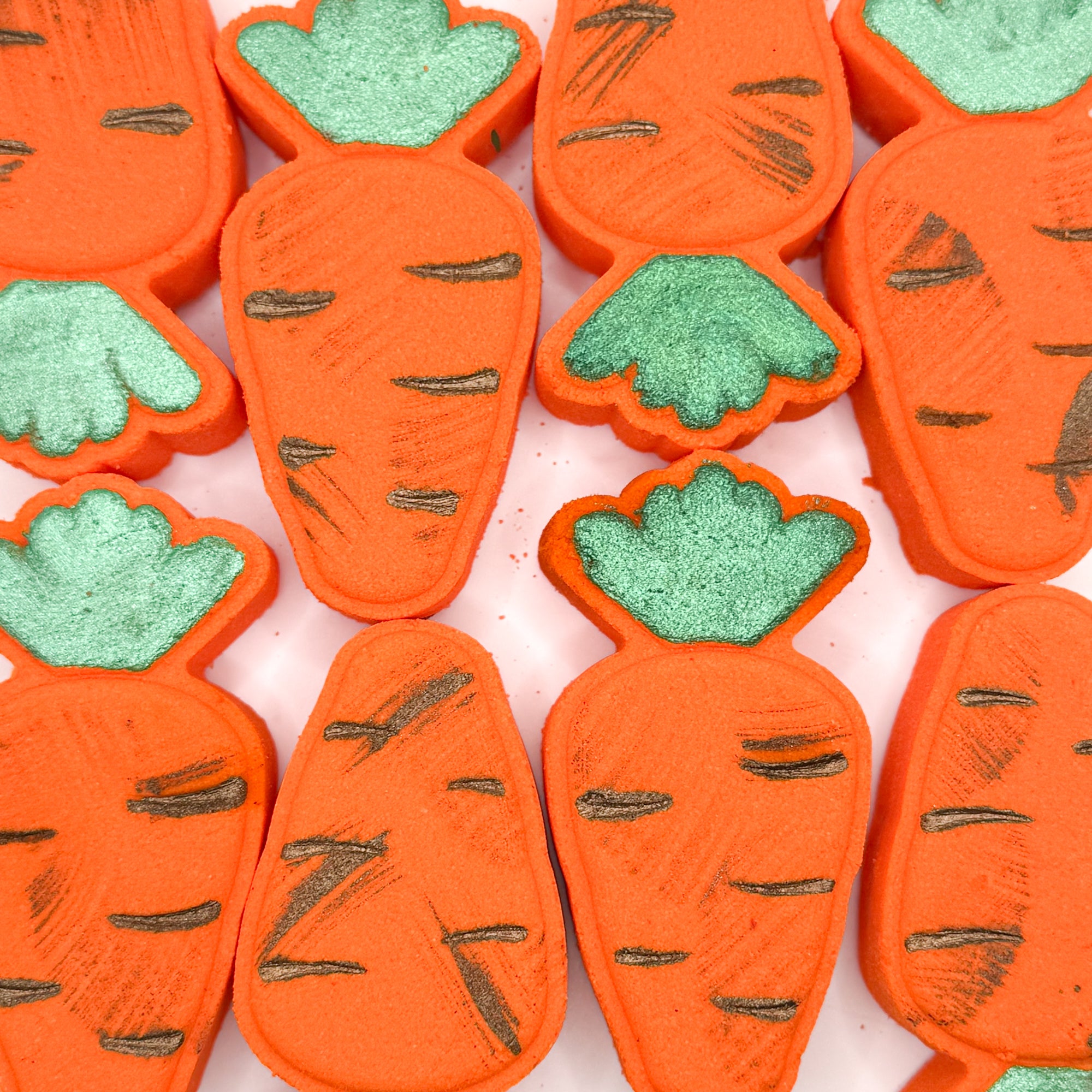 Hand painted orange Carrot shaped bath bombs with green tops and “dirt” paint on a white background