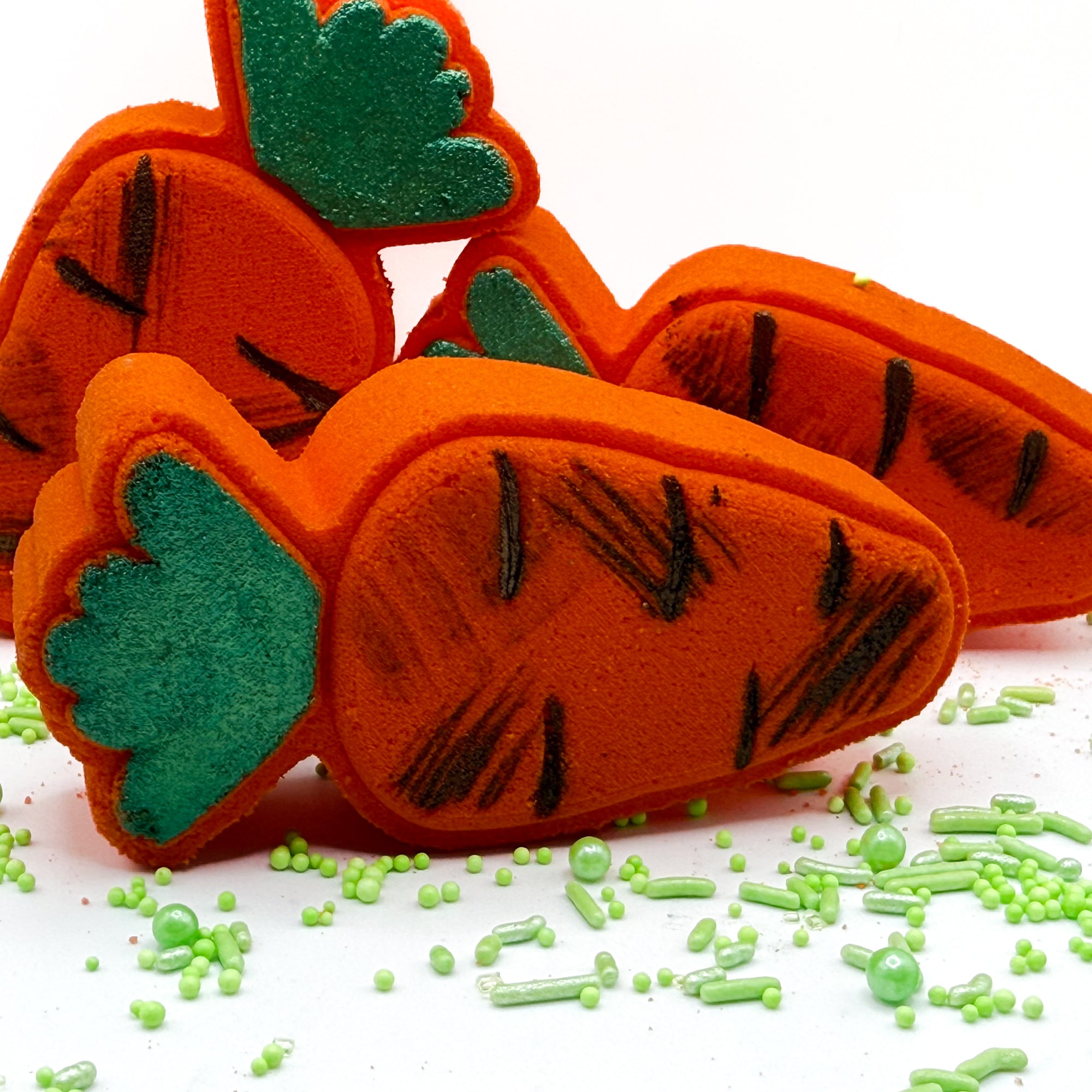 Three orange Carrot  bath bombs hand made by Rusted Acre Soap Co with painted green tops and “dirt” paint on a white background