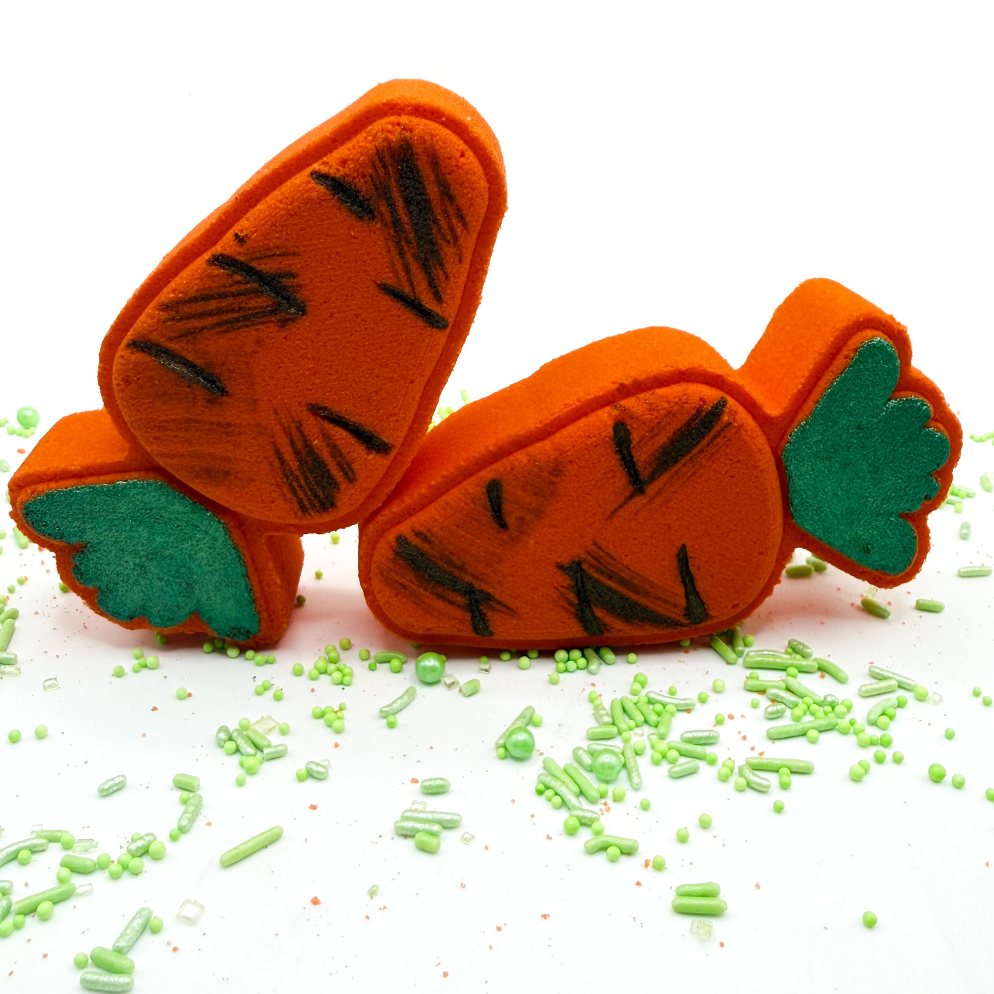 Two handmade orange Carrot bath bombs with hand painted green tops and “dirt” paint on a white background.