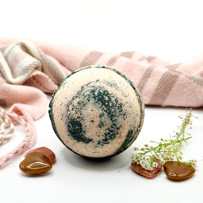 One tan and black round bath bomb on a white  background with a scarf and brown stones. 