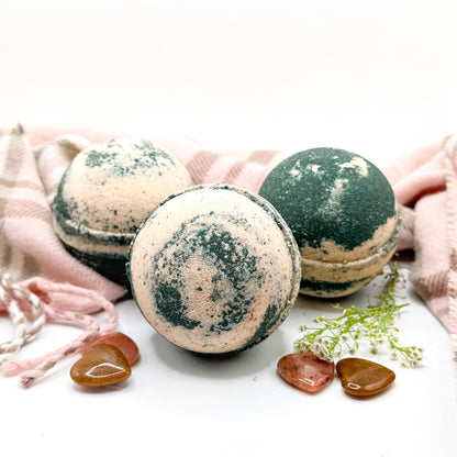 Three black and tan bath bombs surrounded by a scarf and heart shaped stones  