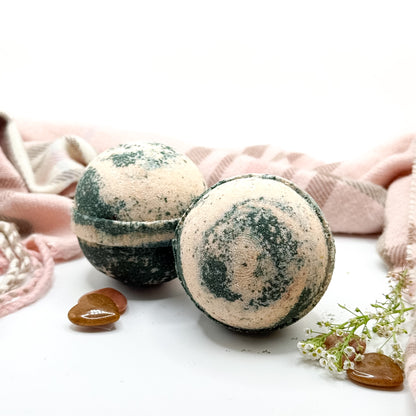Two tan and brown cashmere bath bombs on a white background with a scarf and flower and tan stone hearts. 