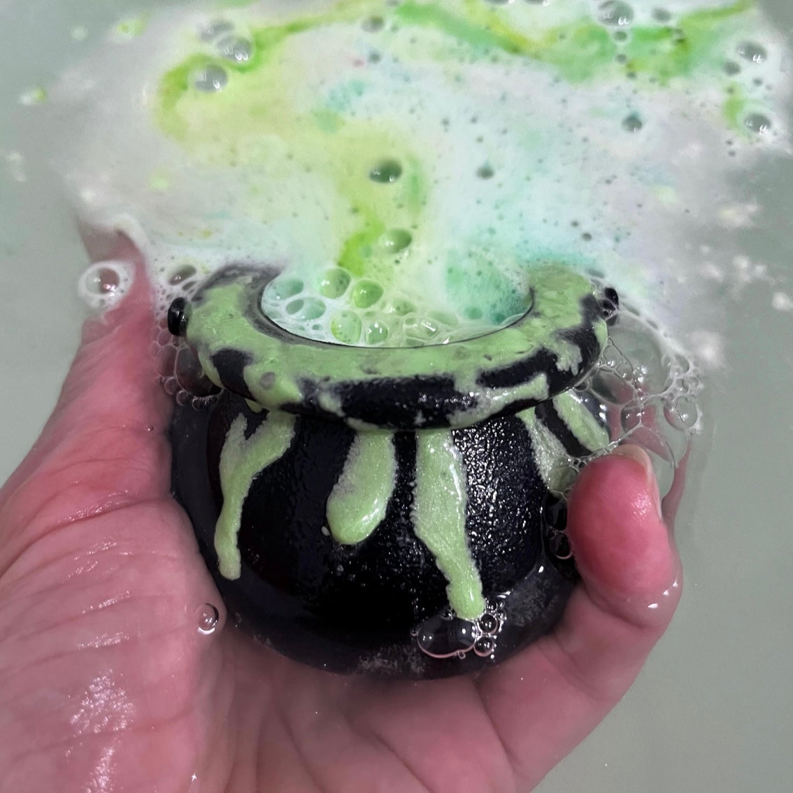 Cauldron bath bomb in the water with green bubble frosting dissolving in the water. 