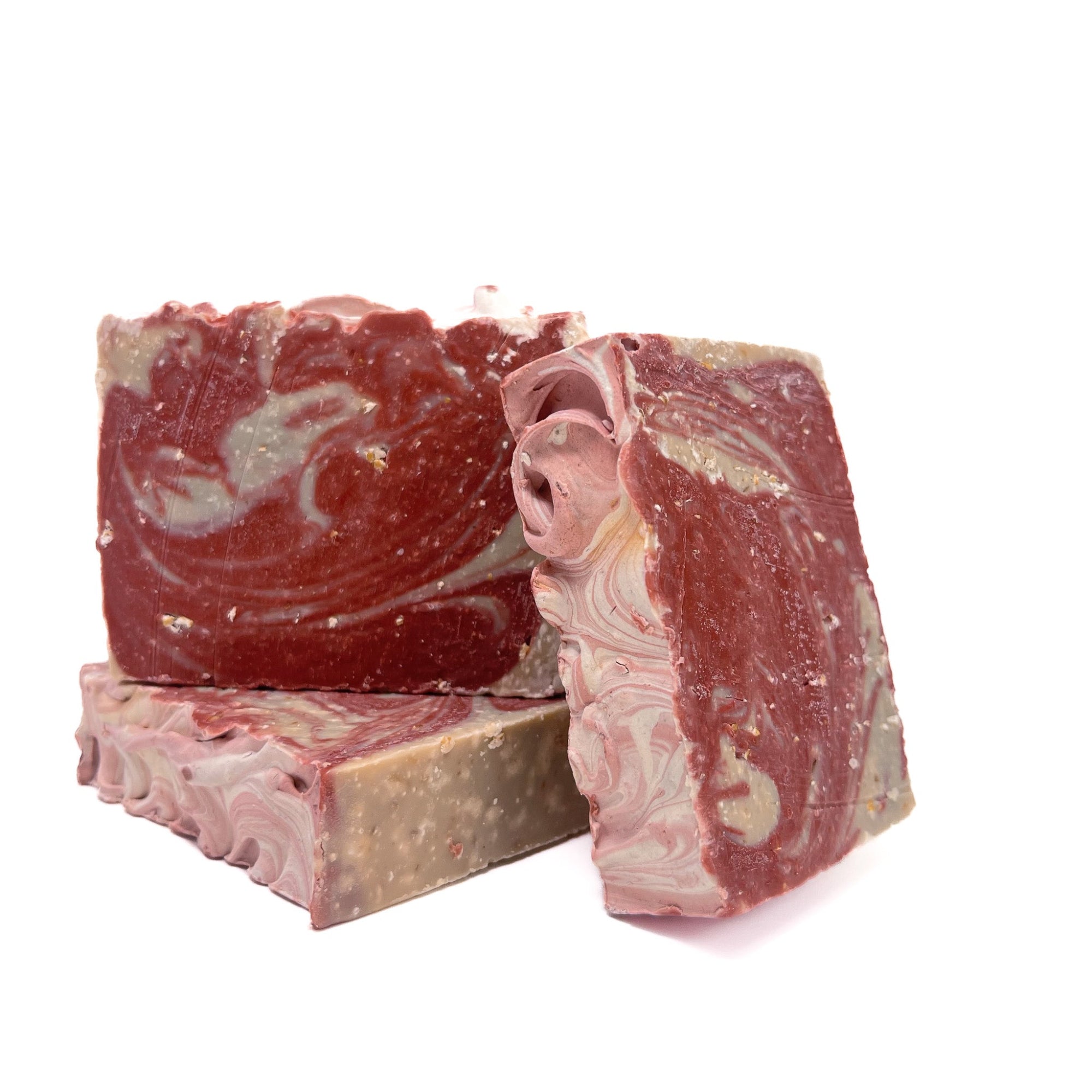 Three bars of red and natural white swirled handmade soap scented with cherry almond from Rusted Acre Soap Co. Two top facing photo to show texture.