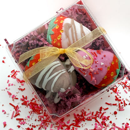 Multiple chocolate covered strawberry bath bombs hand made by Rusted Acre Soap Co with pink, white and brown chocolate hand dipped to look regular strawberries packaged in a gift box with a gold bow. 