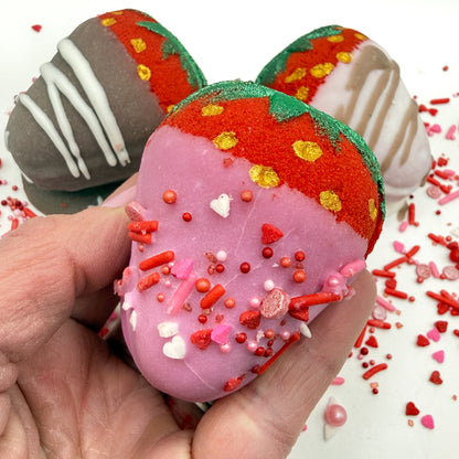 Chocolate covered strawberry bath bomb with pink “chocolate” and sprinkles, held by a hand.