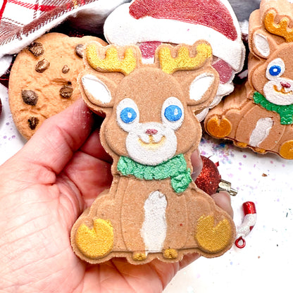 Hand holding a hand painted reindeer shaped bath bomb with other decorated bath bombs in the background