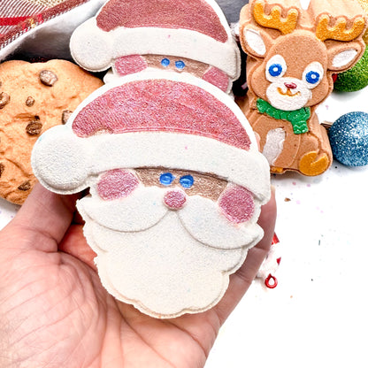 Hand holding a hand made Santa Claus bath bomb with other Christmas-themed bath bombs in the background.