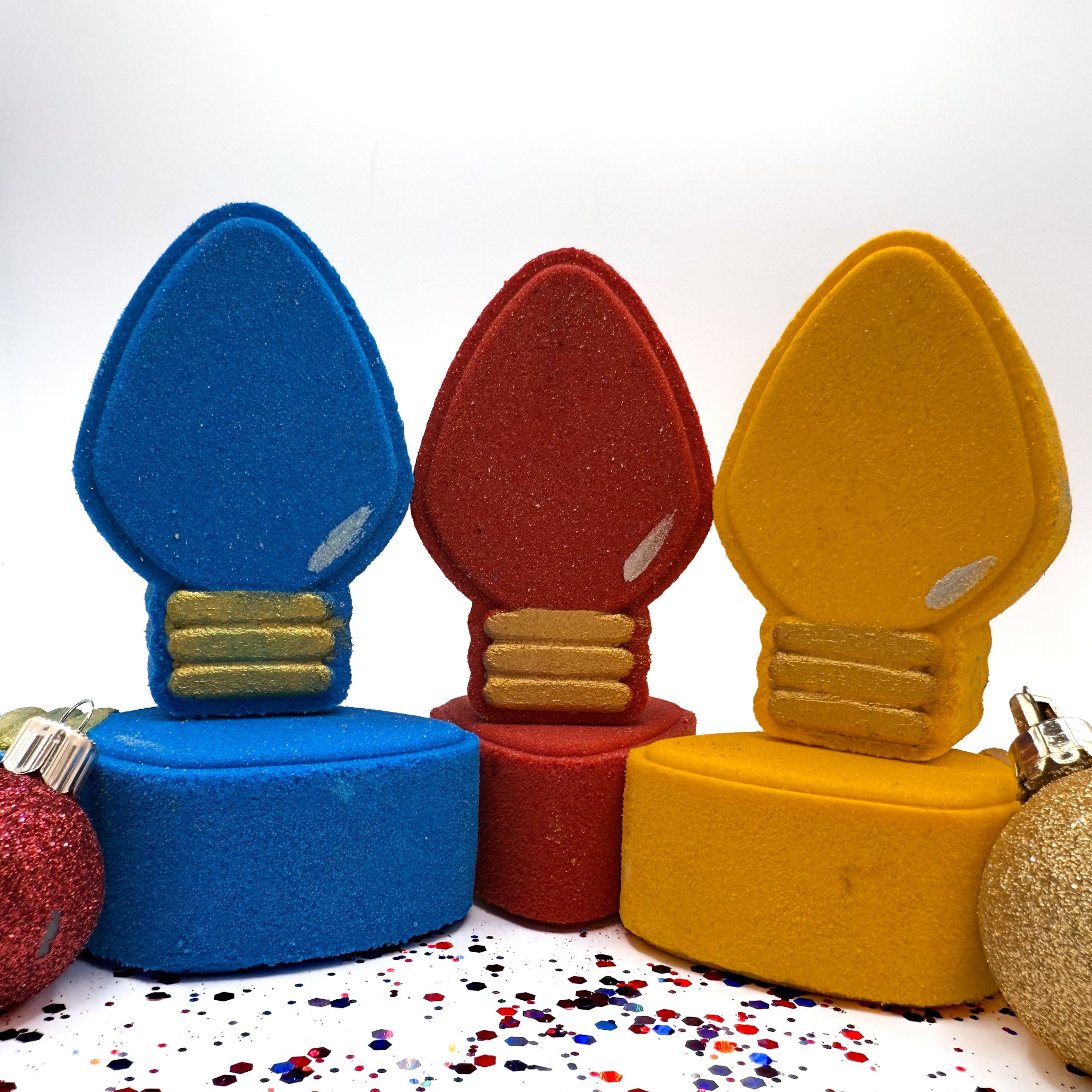 Colorful light bulb shaped Christmas bath bombs on a white background with confetti.