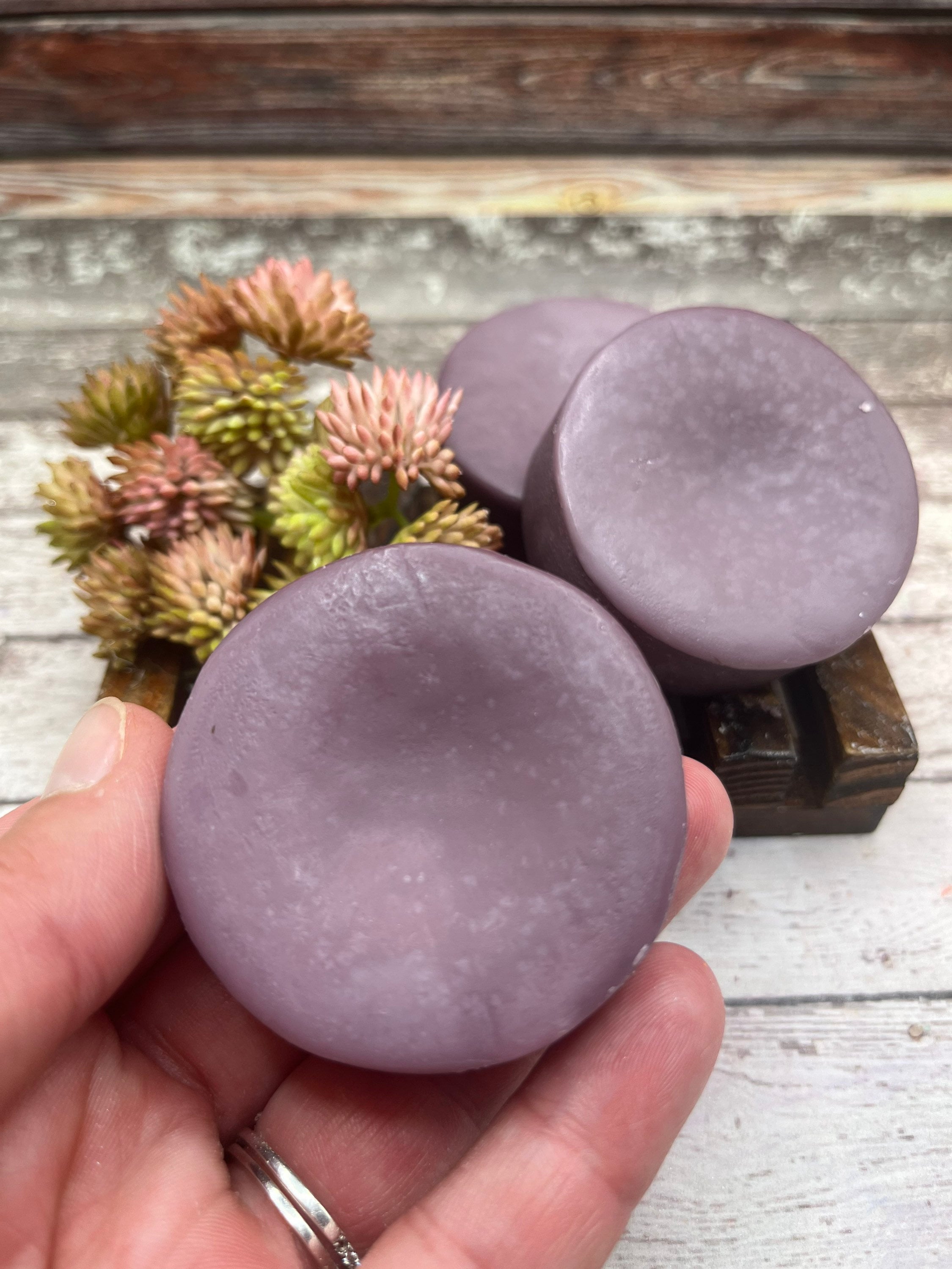 Lavender colored circular shaped conditioner bar in a hand.