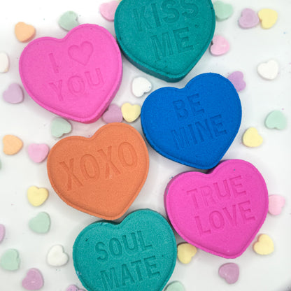Colorful heart shaped bath bombs with conversation heart candies sayings on a white background