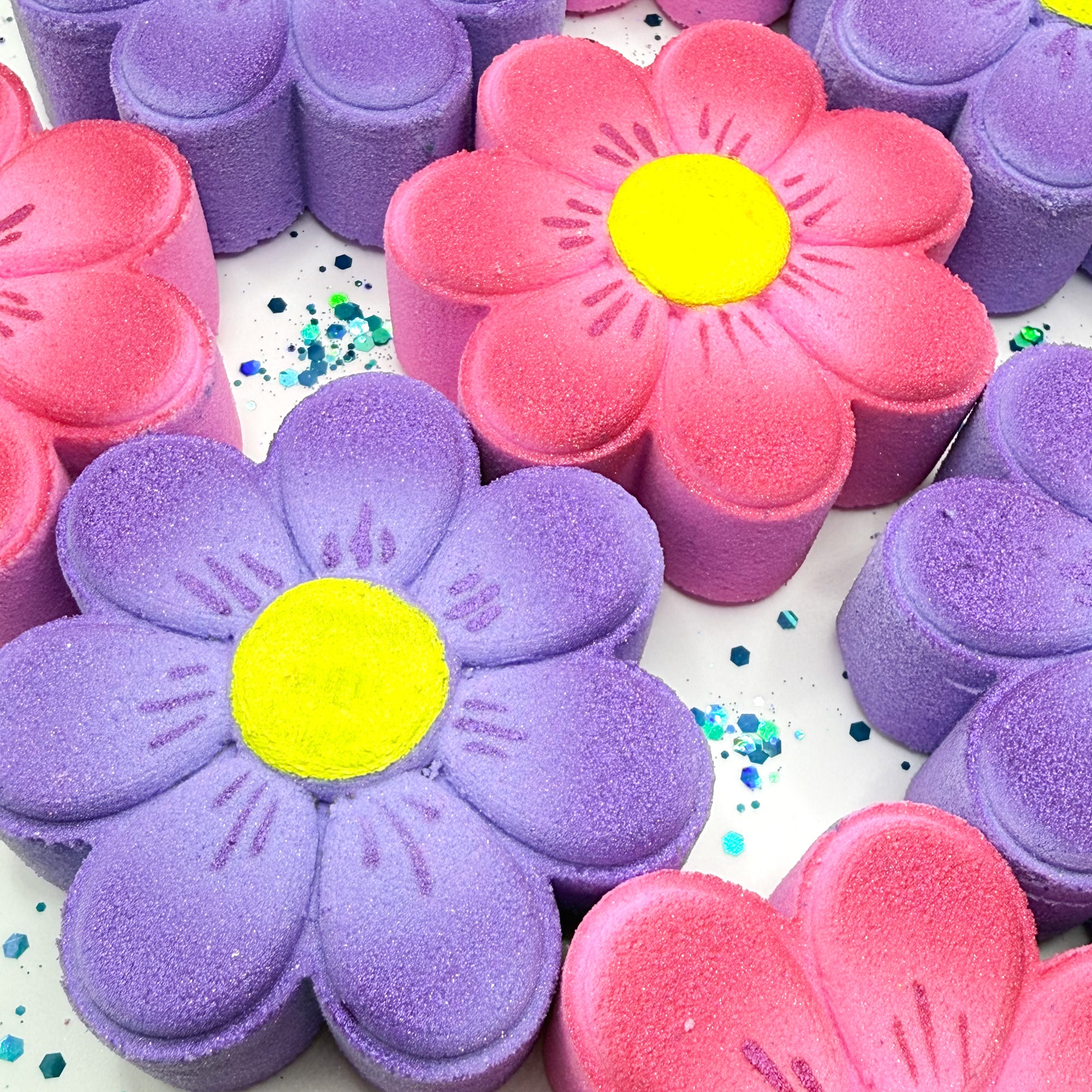 Colorful daisy bath bombs with pink and purple flowers and yellow centers on a white background.
