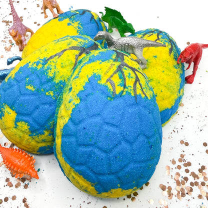 Blue and yellow dinosaur egg bath bombs with toy dinosaurs on a white background