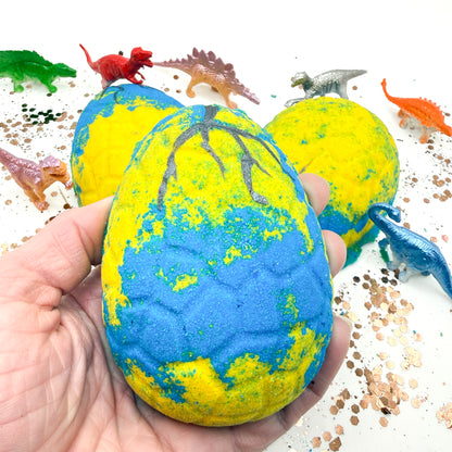 Blue and Yellow dinosaur egg bath bomb with dinosaur figures on a white background hand made by rusted acre soap co. 