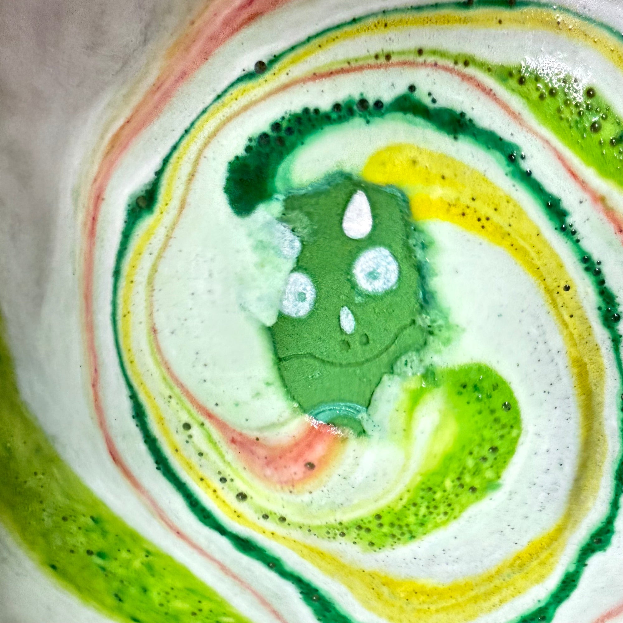 Rusted Acre soap Companies Dinosaur egg bath bomb in the water with a swirl of yellow, green and red colors and foam.