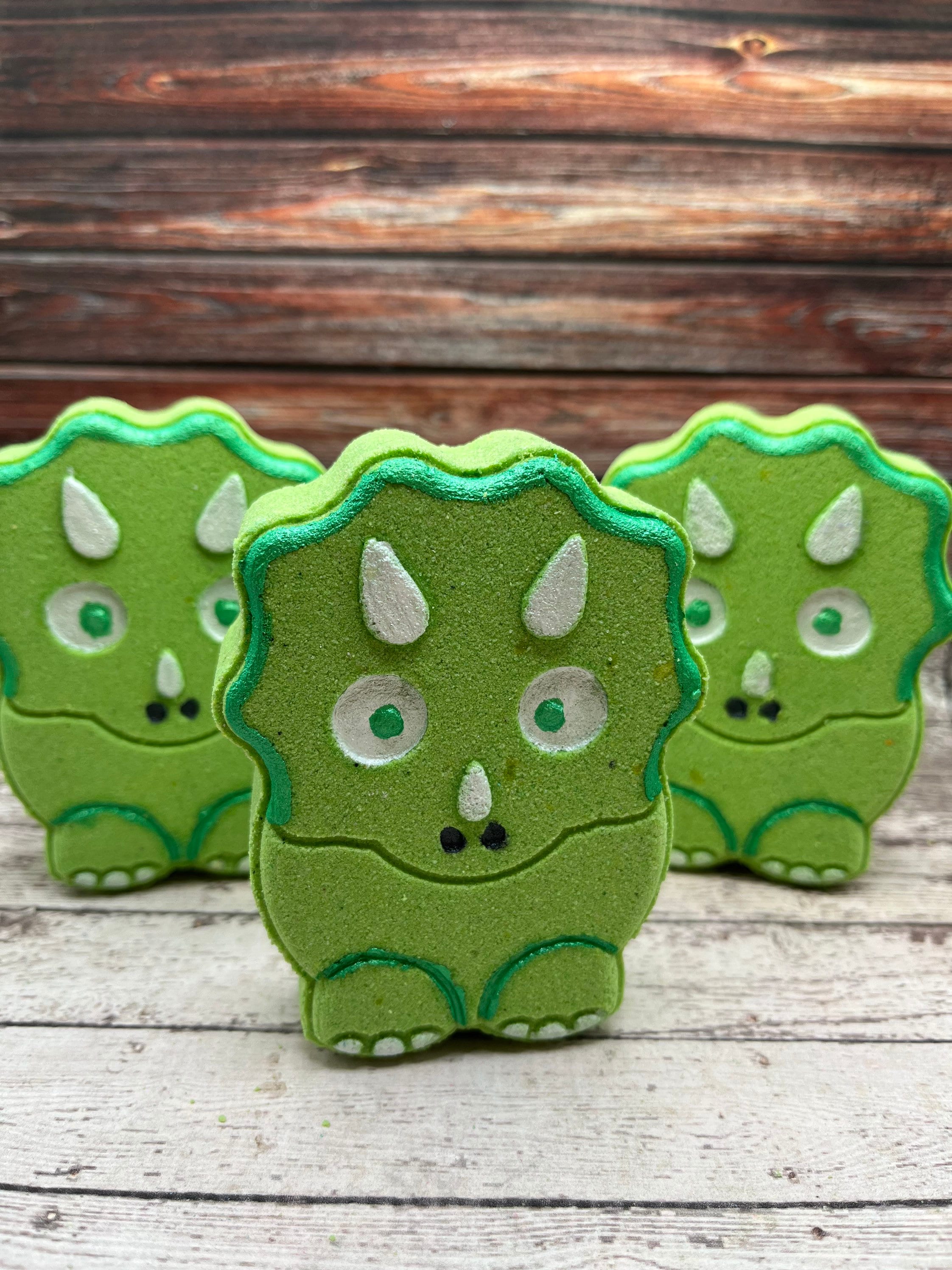 Three green dinosaur shaped bath bombs. Hand-painted white eye brows and nose along with green eyes and outlined in green. 
